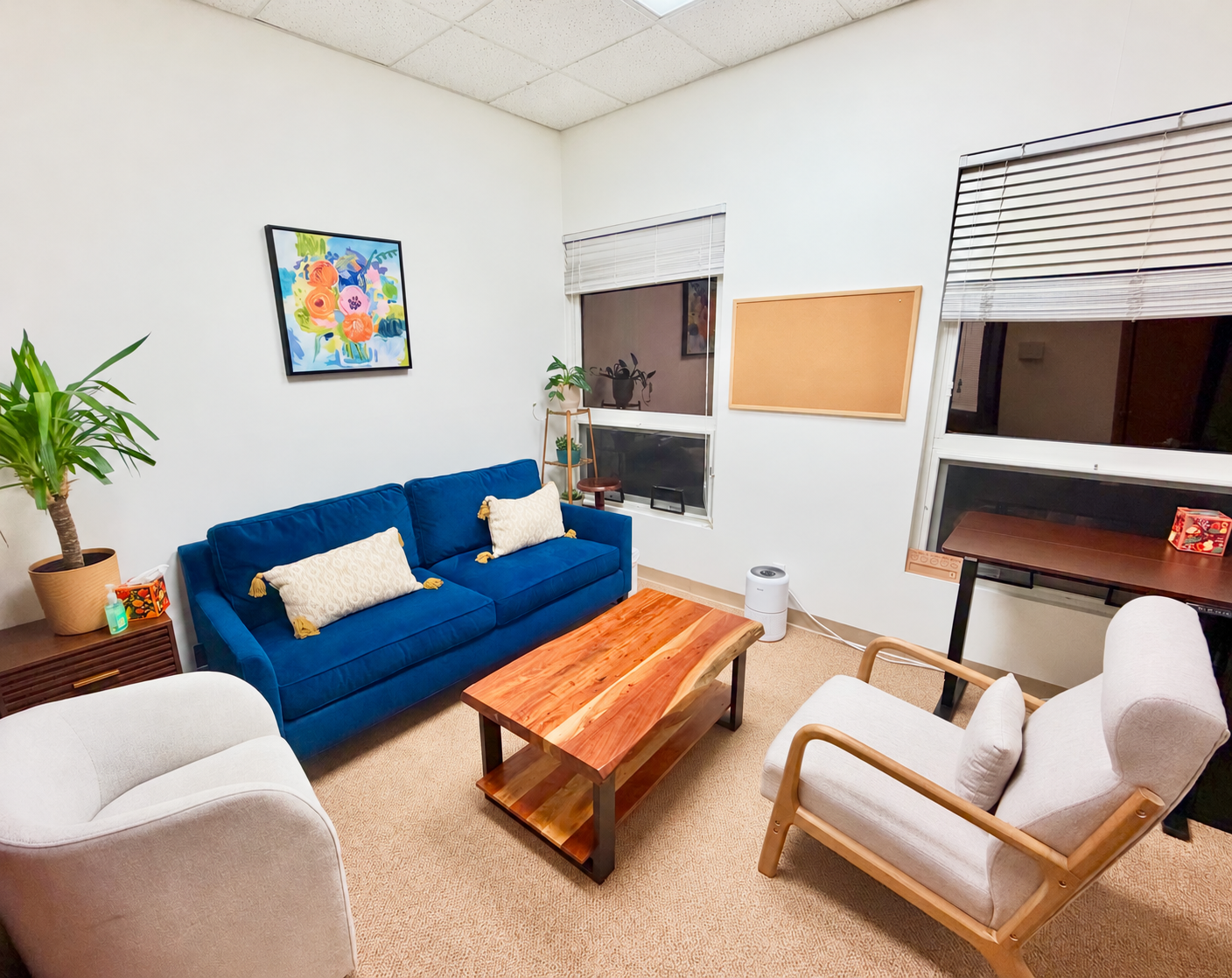 Debi’s therapy office, with a blue sofa, comfortable armchairs, warm wood furniture, and plants